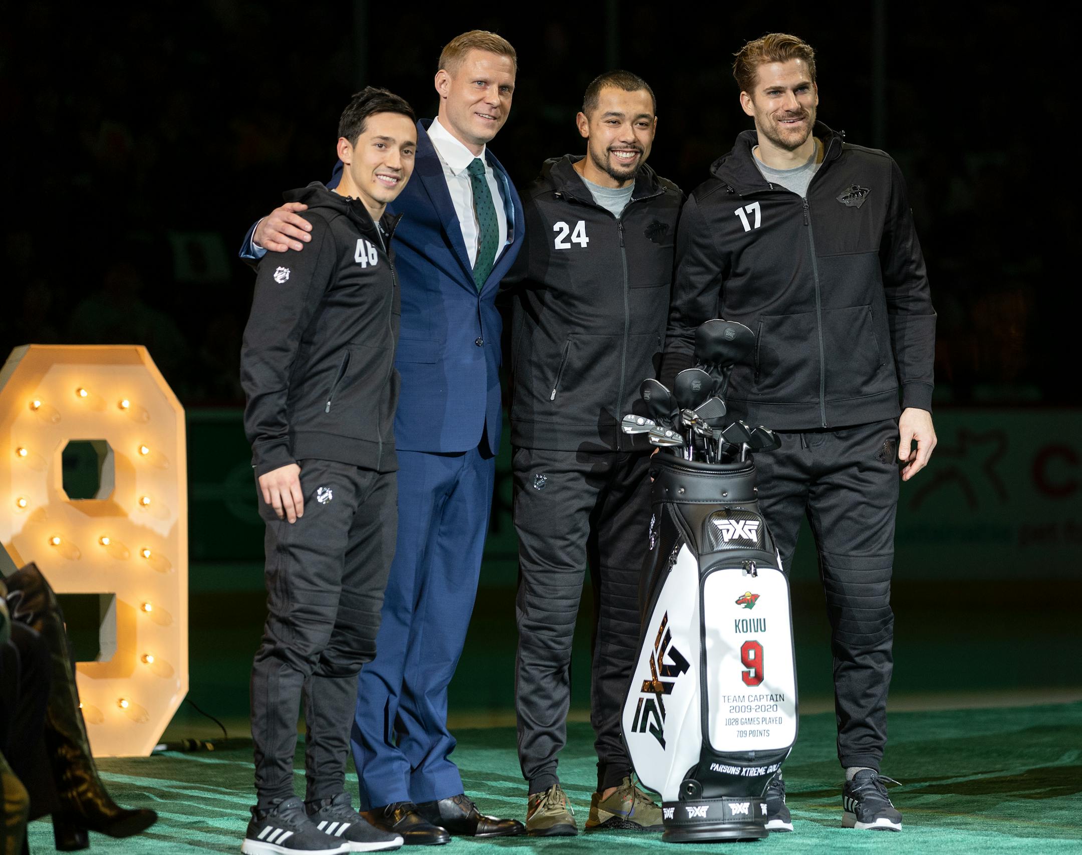 Jared Spurgeon, Mikko Koivu, Matt Dumba and Marcus Foligno pose for a photo with a set of golf clubs that were given to Koivu during a ceremony to retire his number.