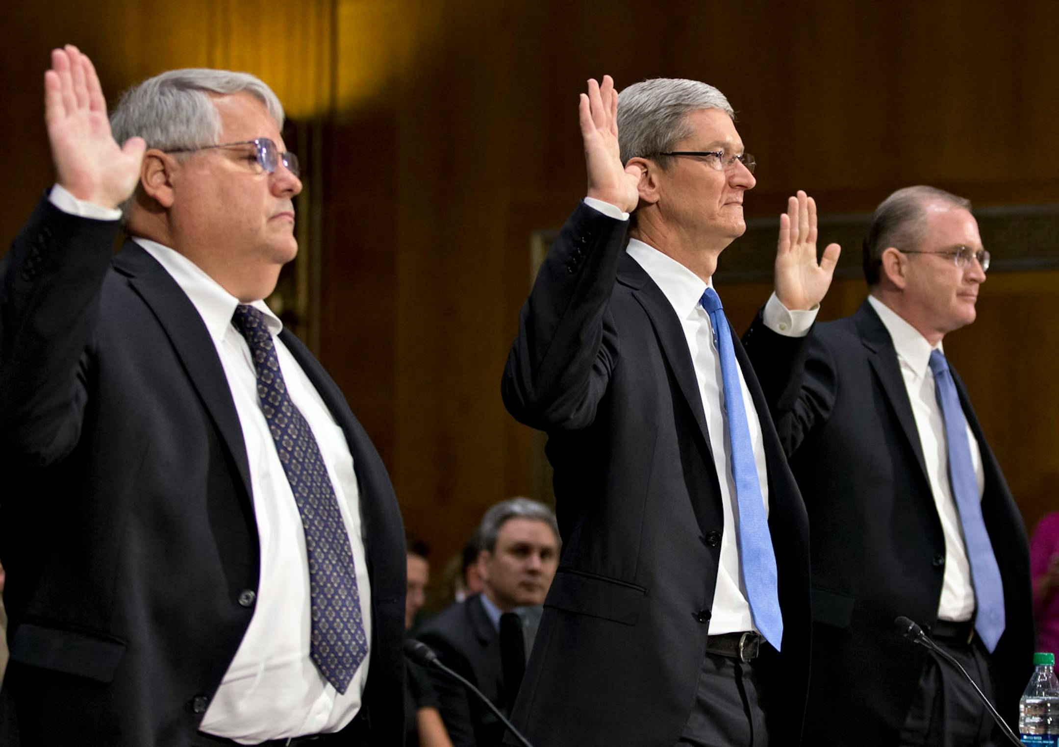 Apple CEO Tim Cook, center, flanked by Peter Oppenheimer, Apple's chief financial officer, left, and Phillip A. Bullock, Apple's head of Tax Operations, are sworn in on Capitol Hill in Washington, Tuesday, May 21, 2013, prior to testifying before the Senate Homeland Security and Governmental Affairs Permanent subcommittee.