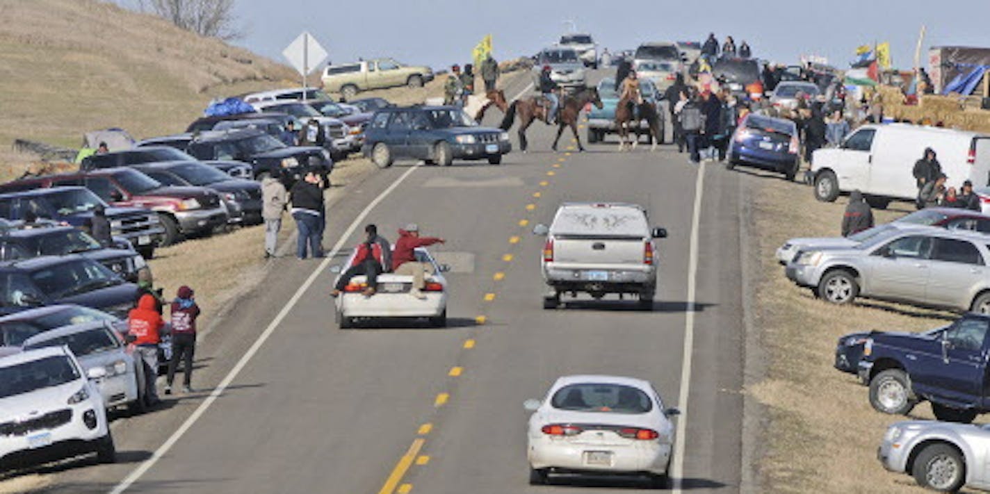 People protesting the Dakota Access Pipeline gather along North Dakota Highway 1806 in Morton County at the site of a new camp that was being put together on Monday, Oct. 24, 2016, in Cannonball, N.D. On Sunday a road block made from rocks, wood and hay bales was put in place but later taken down. The protesters erected tents and teepees on the property along the pipeline route over the weekend. (Tom Stromme/The Bismarck Tribune via AP)