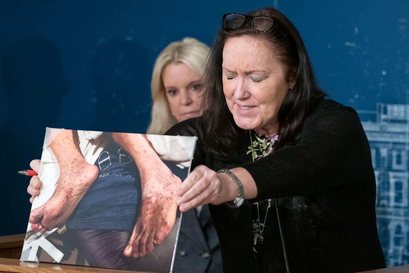 Jane Overby closed her eyes as held a photo with her mother's feet showing a condition that went untreated. Her mother Joan Ziebarth died in a nursing home. With her is Sen. Karin Housley, R-St Marys Point.