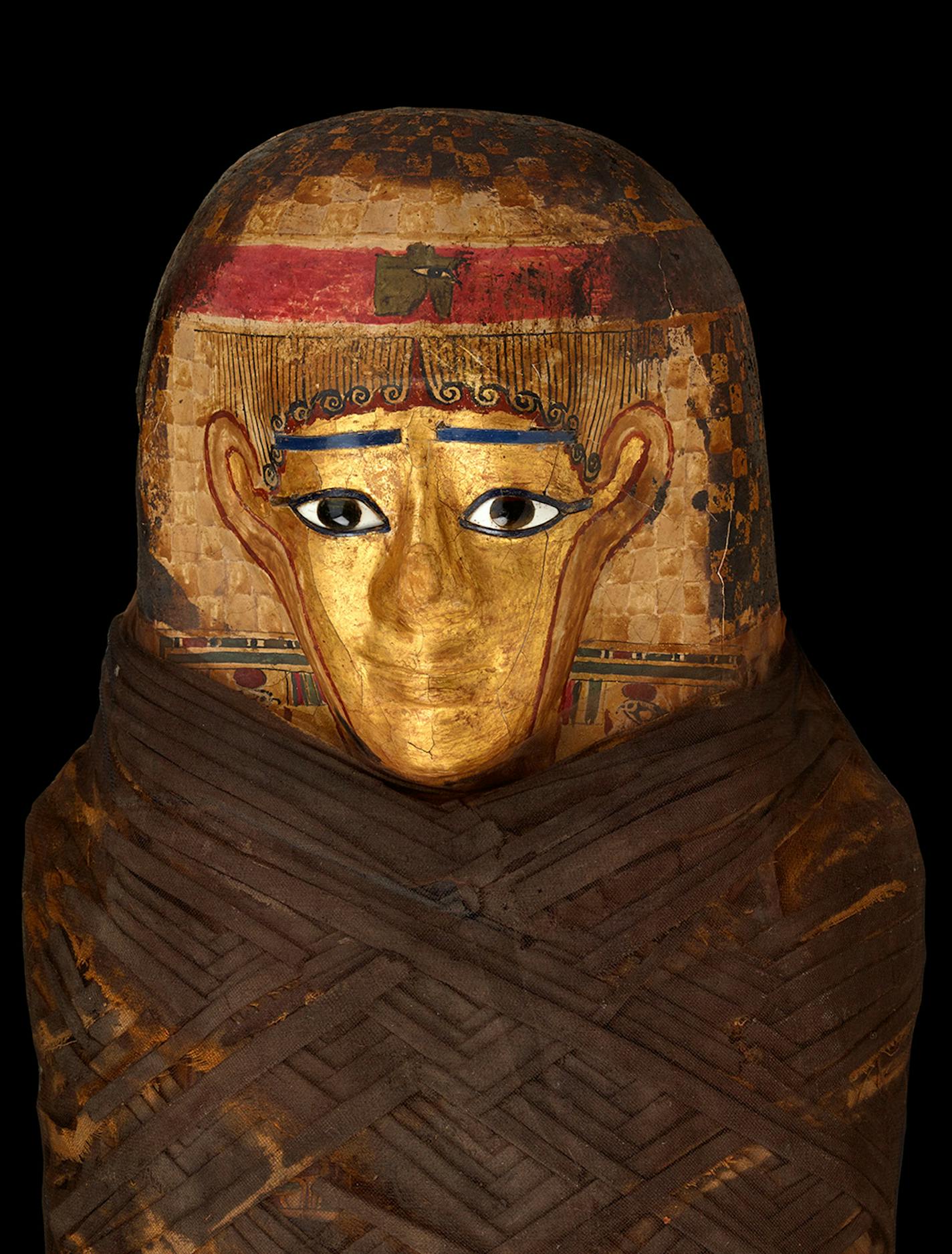 This mummy's headdress is made of cartonnage (glued layers of papyrus or linen) and covered with gilding. Ancient Egyptians believed the gold would enable the deceased's eyes, nose and mouth to remain intact for the afterlife.