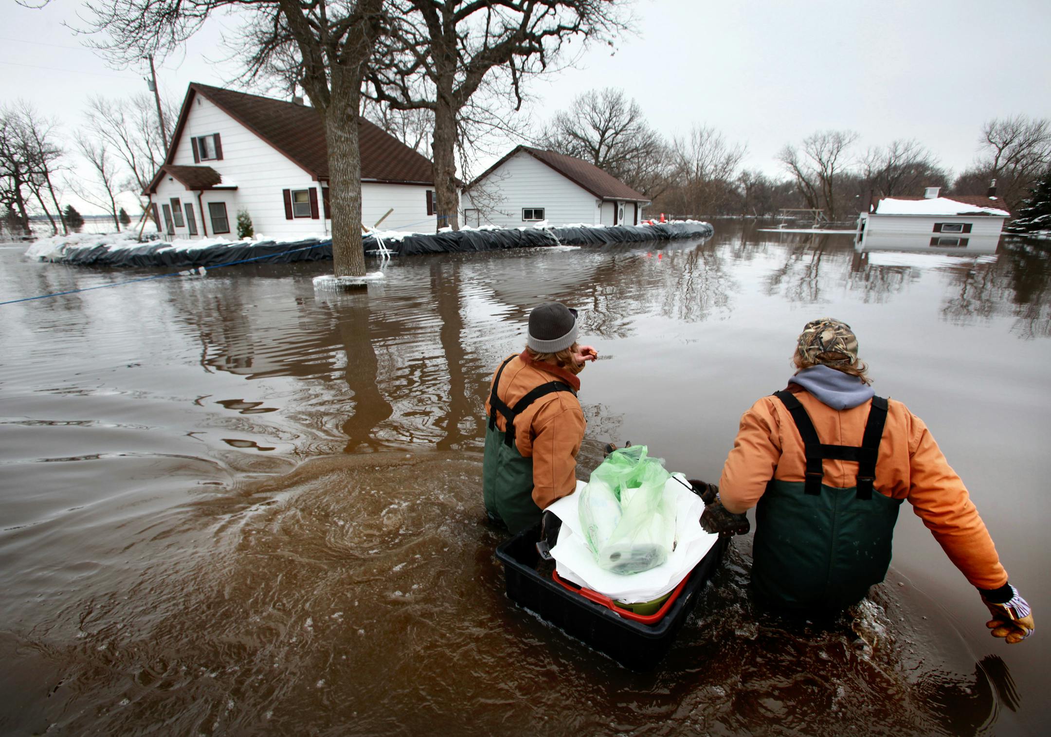 BRIAN PETERSON ï brianp@startribune.com Fargo, ND - 3-29-2009 ] Day Shift - Darrell Schlagel (right) and his son Cody, haul in supplies to the home of their friend Mike Wieser who lives along the WIld RIce RIver south of Fargo. The Weiser home was surrounded by four feet of water but was holding back the flood waters as of Sunday afternoon. Naze and his friends had been taking 24 hour shifts to protect the house and keep the pumps going.