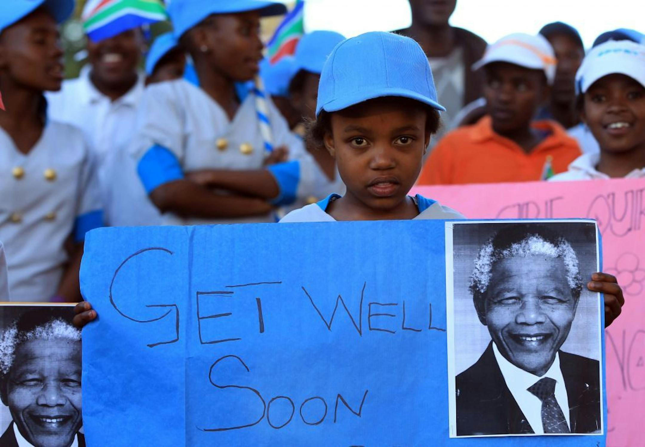 Soweto African kids hold posters and prints and get well messages outside the home of the former President Nelson Mandela in Johannesburg, South Africa, Saturday, June 15, 2013. Mandela, remains in the hospital for a seventh day. The 94-year-old was hospitalized on Saturday for a recurring lung infection.