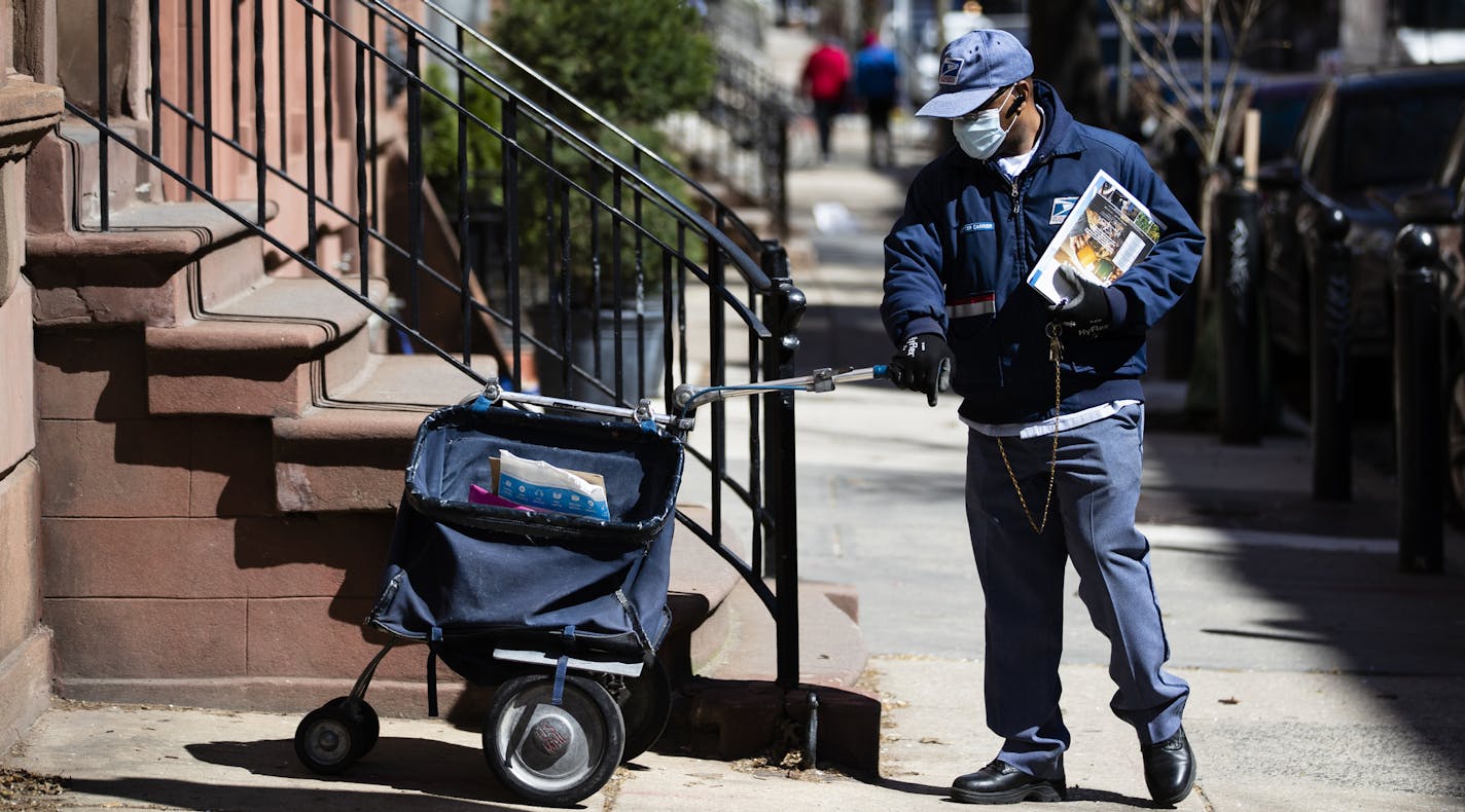 A United States Postal worker makes a delivery with gloves and a mask in Philadelphia, Thursday, April 2, 2020. The U.S. Postal Service is keeping post offices open but ensuring customers stay at least 6 feet (2 meters) apart. The agency said it is following guidance from public health experts, although there is no indication that the new coronavirus COVID-19 is being spread through the mail. (AP Photo/Matt Rourke)