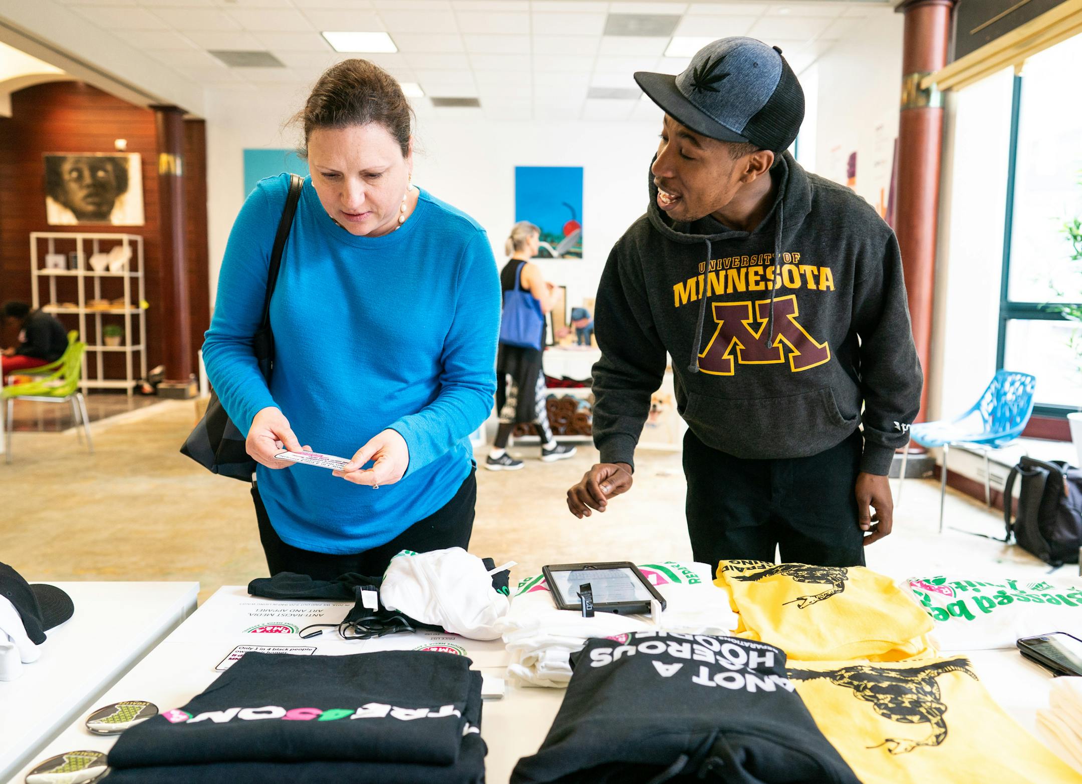 Noel Gordon Jr. walks Sara Barrow though items by Reparations Media and Apparel. Gordon, a graduate student and the University of Minnesota's Carlson and Humphrey schools, said the brand uses humor to point out absurdity if racial inequality in America while providing a sustainable income to creators of color. ] MARK VANCLEAVE &#xa5; The Chameleon Consortium pop-up retail spaces in Gaviidae Commons launched Monday, Apr 1, 2019. About 20 primarily minority-led small business will filling the stre