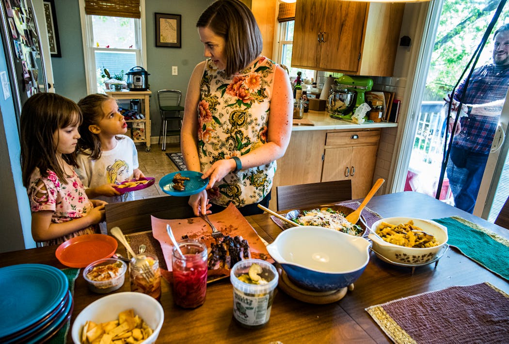 Calley Graham helps Addie Haugen, 7, and her daughter, Frankie, 5, with plating some brisket as Steve McPherson walks in the kitchen. A year and a half after the neighbors created a so-called “pandemic pod” to socially isolate themselves from the outside world, they’re continuing to enjoy their friendships and rely on one another.
