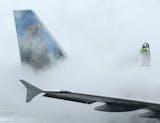 A crewmember de-ices a Frontier Airlines plane at LaGuardia Airport in New York, Monday, Jan. 26, 2015. More than 5,000 flights in and out of East Coast airports have been canceled as a major snowstorm packing up to three feet of snow barrels down on the region.