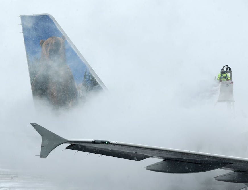 A crewmember de-ices a Frontier Airlines plane at LaGuardia Airport in New York, Monday, Jan. 26, 2015. More than 5,000 flights in and out of East Coast airports have been canceled as a major snowstorm packing up to three feet of snow barrels down on the region.