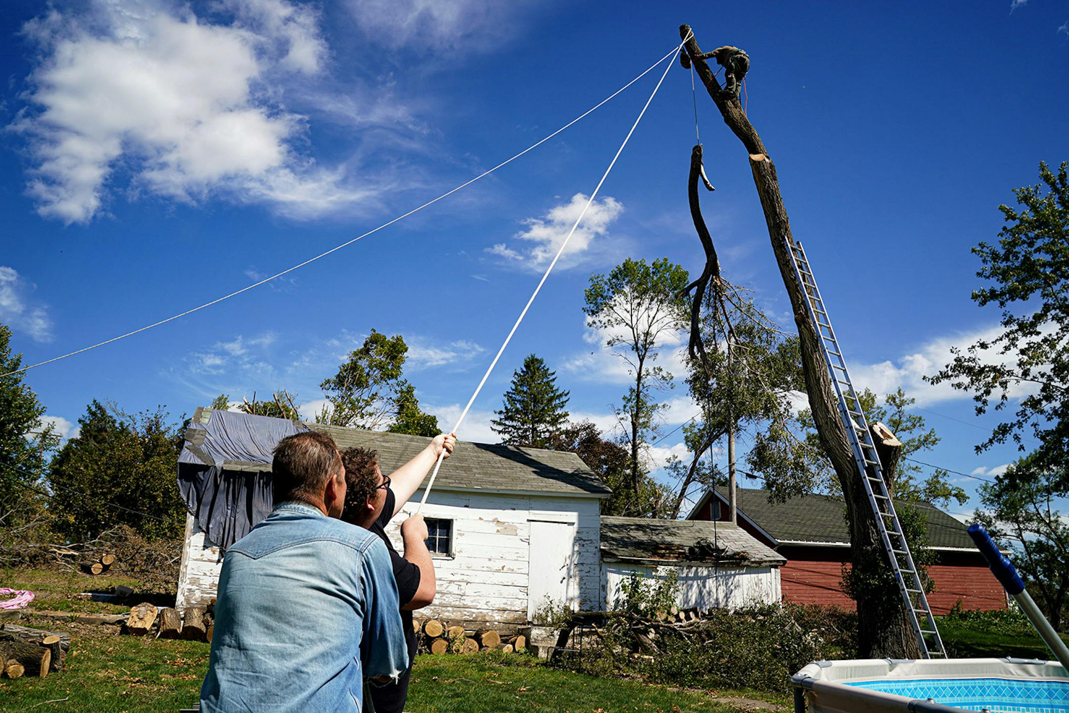 Tama, Iowa homeowner Sam Brewer, right and his father Joe Brewer held a line to help Dan Clay remove a branch from a damaged tree. The branch was hanging over Brewer's shed and was removed successfully. Winds up to 100 miles per hour ripped up trees and crops last week through much of central Iowa.