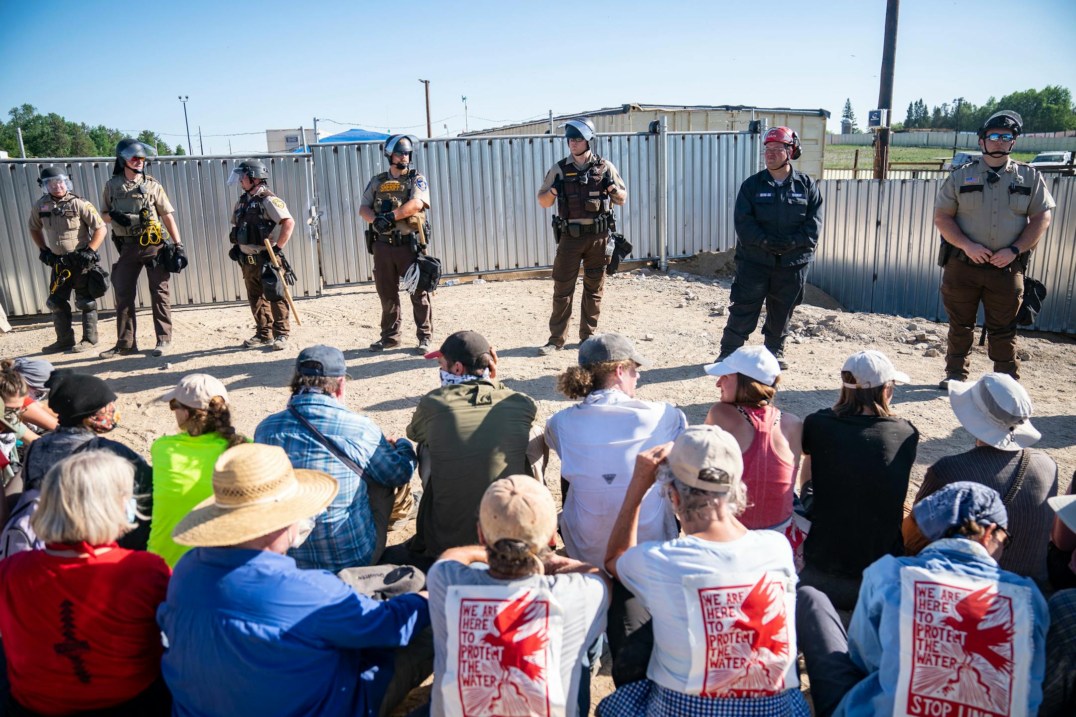 Law enforcement agents formed a line in front of a wall of protestors who sat just in front of a locked gate at an Enbridge pump station on Monday.