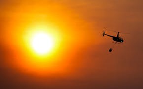 A helicopter carries a bucket as it flies over homes burned by the Smokehouse Creek Fire, Wednesday, Feb. 28, 2024, in Canadian, Texas.