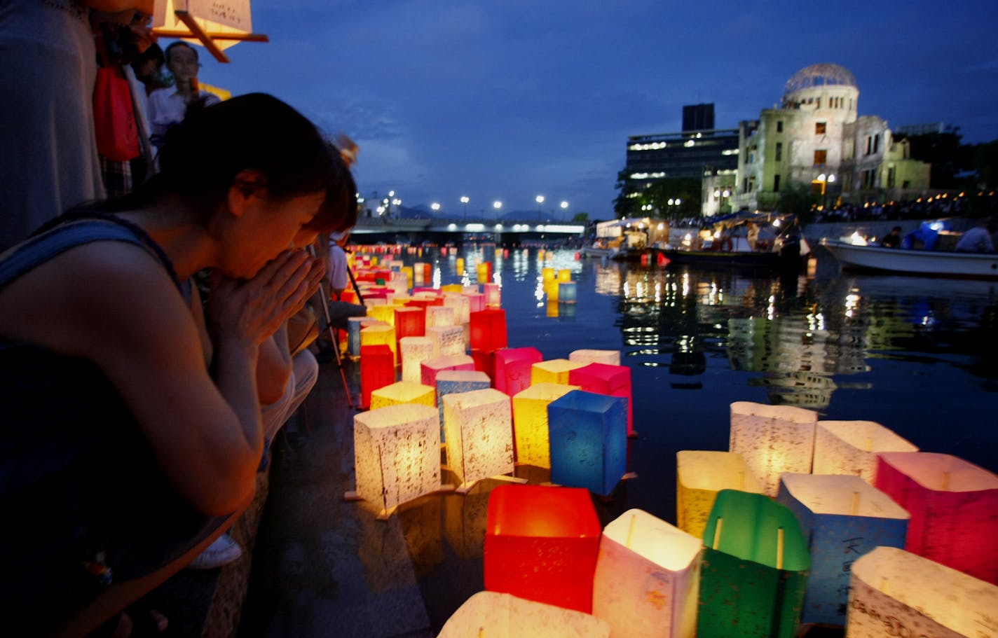 A woman offers prayers as she releases a paper lantern in the Motoyasu River with the backdrop of the Atomic Bomb Dome in Hiroshima, western Japan, Thursday, Aug. 6, 2009. Hiroshima's mayor urged global leaders on Thursday to back President Barack Obama's call to abolish nuclear weapons as Japan marked the 64th anniversary of the world's first atomic bomb attack. (AP Photo/Shizuo Kambayashi)