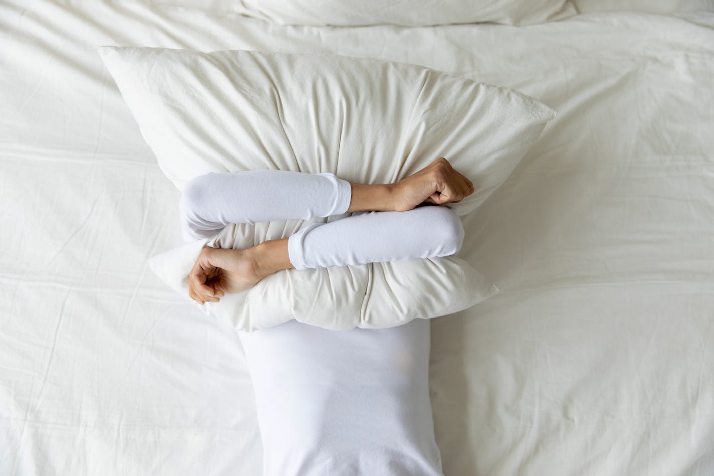 Top view depressed woman covering face with pillow, lying on bed at home alone, frustrated unhappy young female suffering from insomnia, mental or relationship problems, break up or divorce