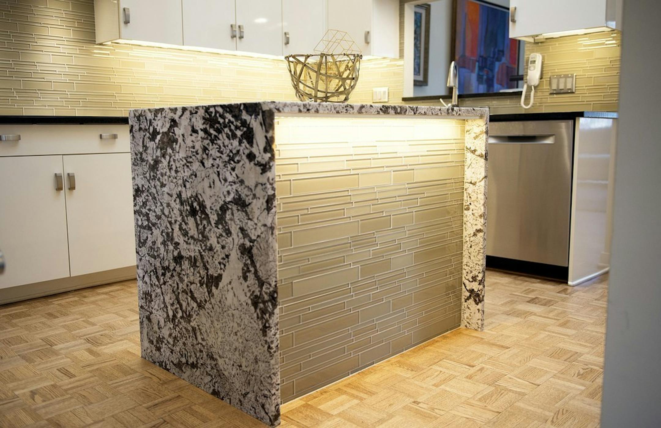 A 1980s kitchen makeover features an island wrapped in granite and mosaic glass tile.