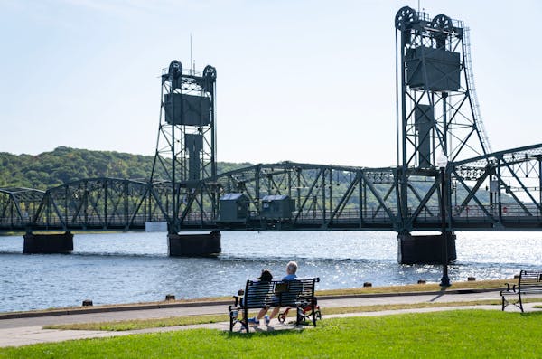 People lounge on a bench and look out at the St. Croix River and historic Stillwater Lift Bridge Thursday, Sep. 14, 2023, in Lowell Park in Stillwater