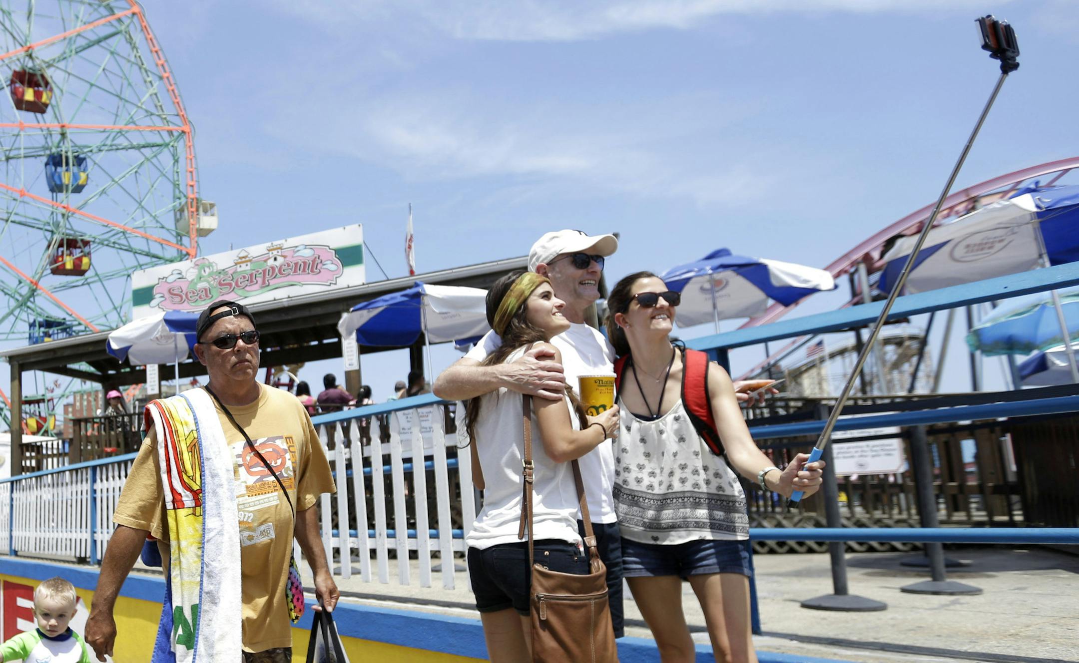 Visitors to Coney Island use a selfie stick to take a photo with the Wonder Wheel in the background, Friday, July 3, 2015, in the Brooklyn borough of New York. Temperatures will be in the mid 70s and 80s for the 4th of July holiday weekend. (AP Photo/Mary Altaffer)