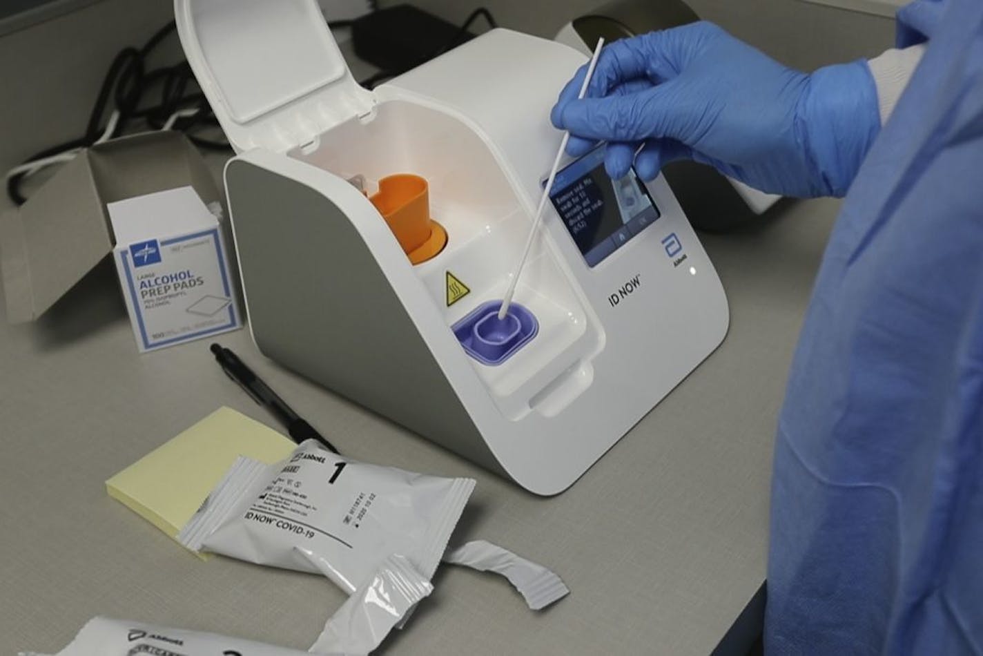 In a frame grab from video, a lab technician dips a sample into the Abbott Laboratories ID Now testing machine at the Detroit Health Center, Friday, April 10, 2020, in Detroit. Dozens of Detroit police officers have been returning to work from the coronavirus quarantine daily due to the speed of the results. Illinois-based Abbott Laboratories says its cartridge-based test, approved last month, delivers results within minutes. "We're prioritizing delivery to outbreak hotspots across the country f