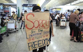 A protester shows a placard to stranded travelers during a demonstration at the Airport in Hong Kong, Tuesday, Aug. 13, 2019. Protesters severely crip