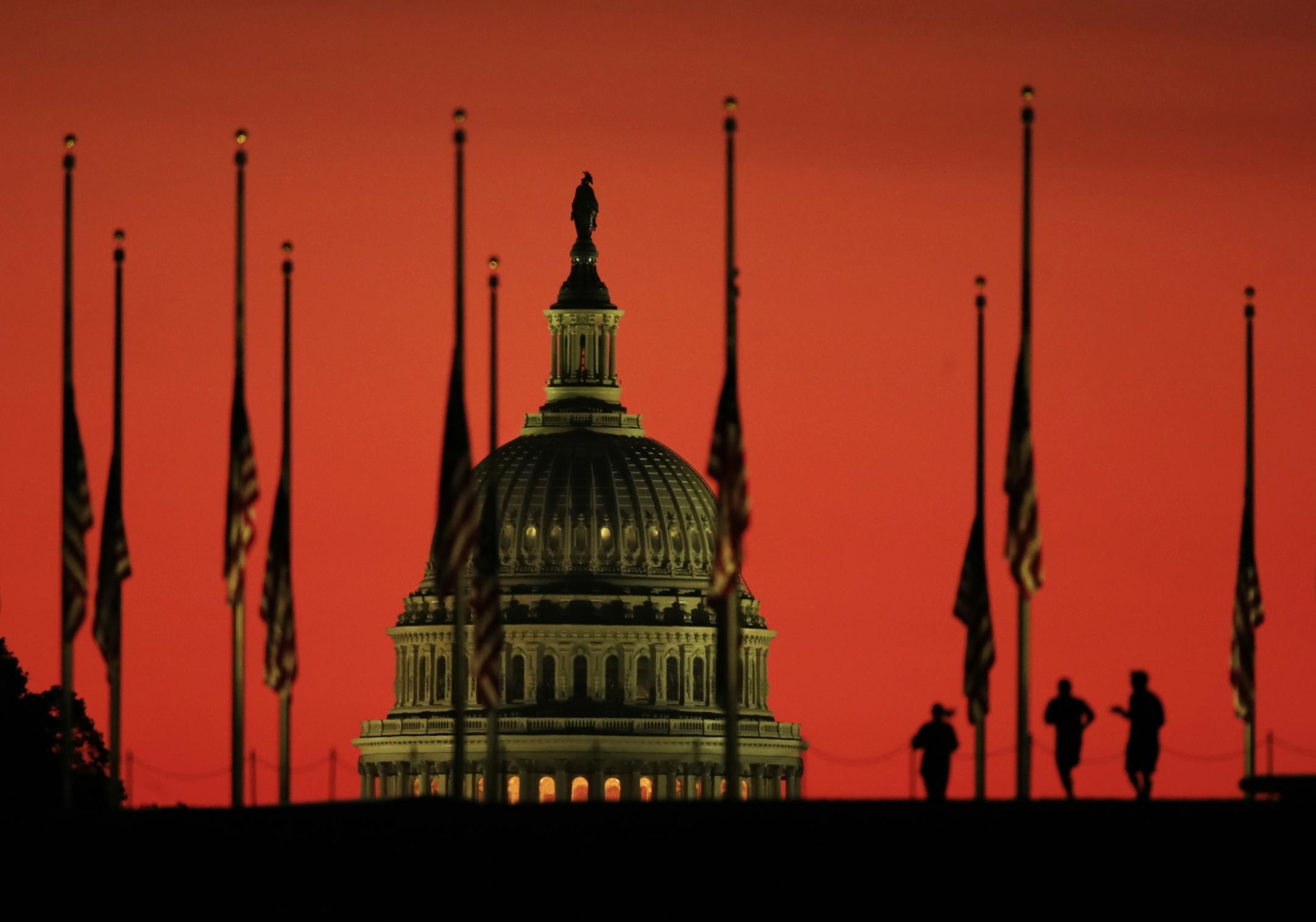 The U.S. Capitol dome backdrops flags at half-staff in honor of the victims killed in the Las Vegas shooting as the sun rises on Tuesday, Oct. 3, 2017, at the foot of the Washington Monument on the National Mall in Washington.