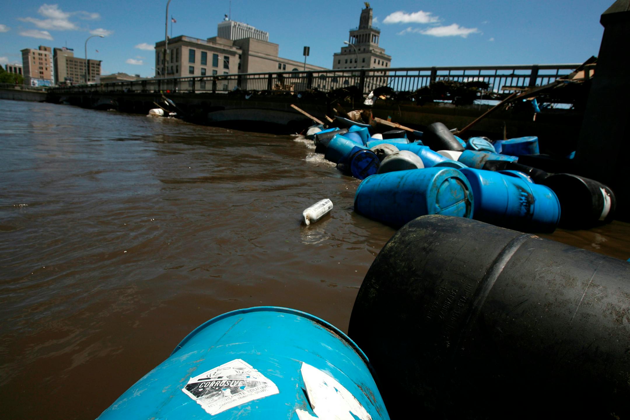 Dozens of barrels, some marked corrosive, jammed up on the Cedar River in Cedar Rapids on Monday. The flood is spreading a noxious brew of sewage, chemicals and gas.
