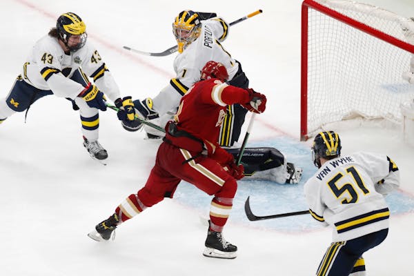 Denver's Carter Savoie (8) gathers the puck for the winning goal on Michigan's Erik Portillo (1) in overtime during an NCAA men's Frozen Four semifina