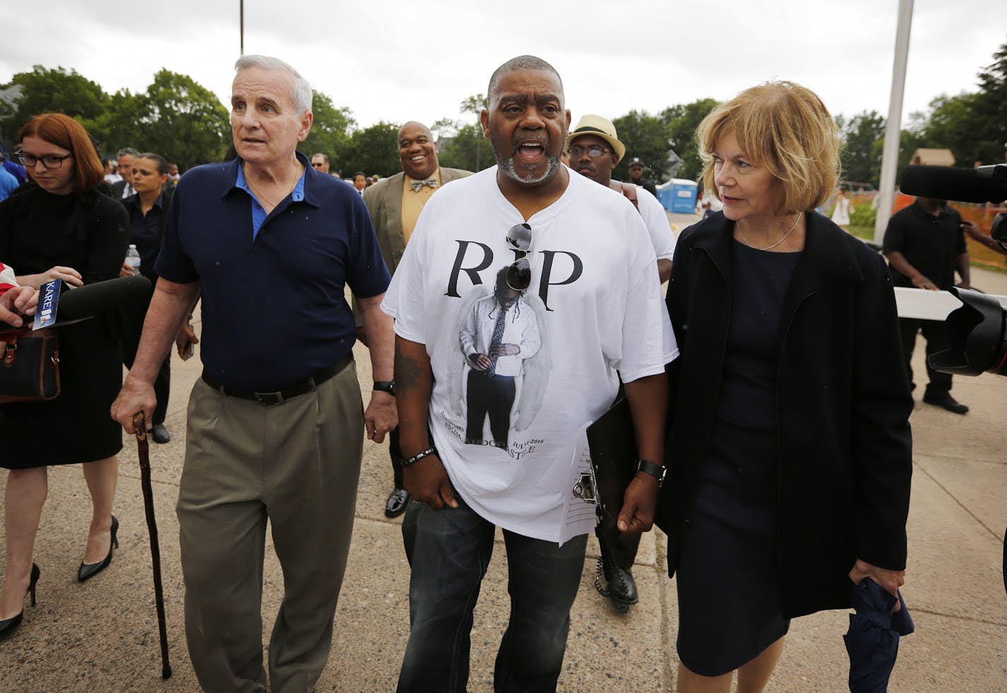 Gov. Mark Dayton and Lt. Gov. Tina Smith walk with Clarence Castile, center, the uncle of Philando Castile, at J.J. Hill Montessori School in St. Paul following the funeral.