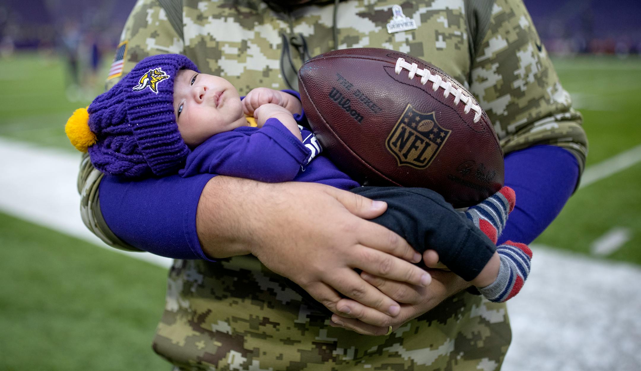 Two-month-old Tre Patterson snuggles in warm hands and a football before the game, Sunday, Nov. 21, 2021 in Minneapolis. Patterson is the son of assistant running back coach AC Patterson.