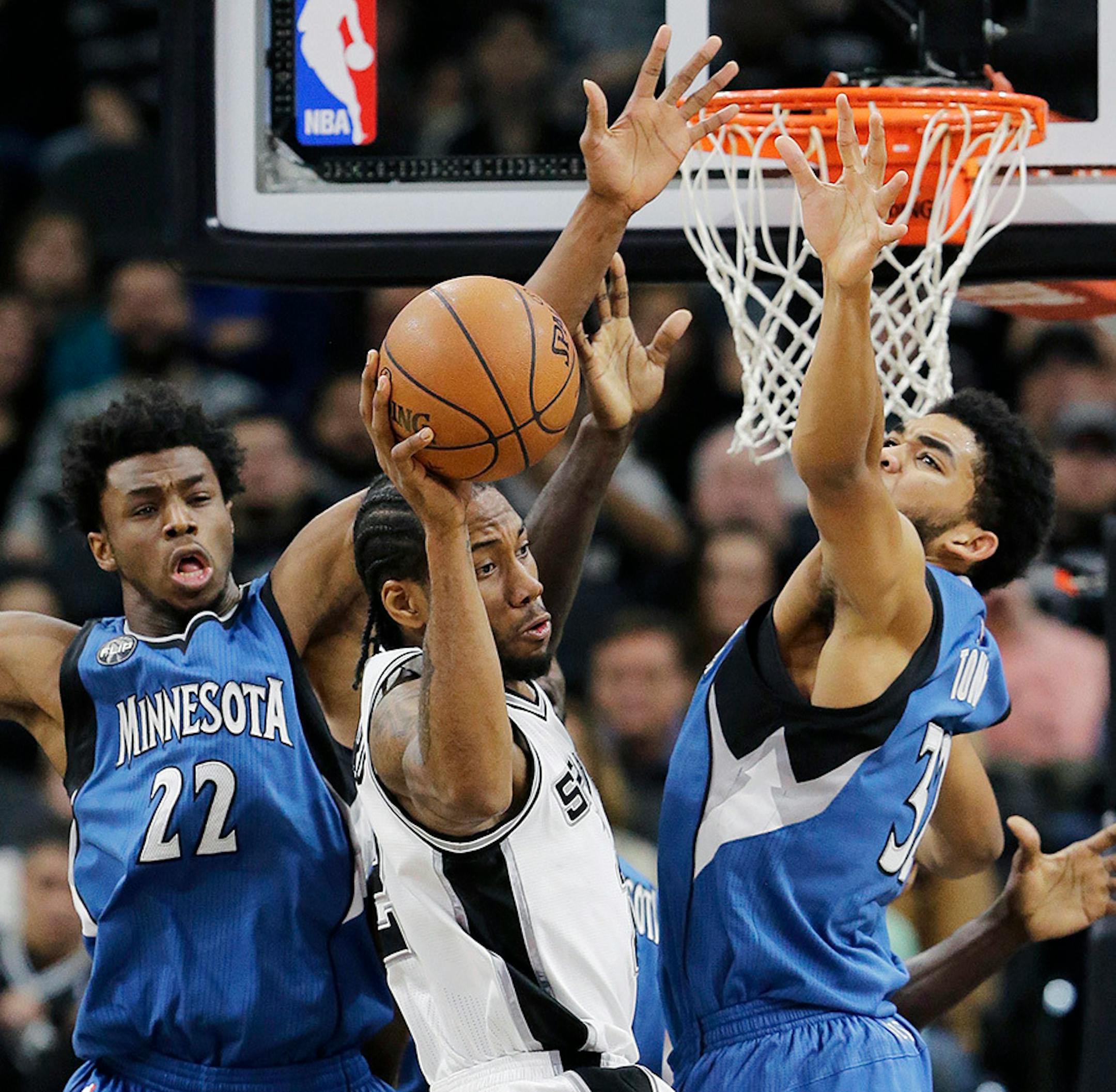 San Antonio Spurs forward Kawhi Leonard, center, passes the ball as Minnesota Timberwolves guard Andrew Wiggins (22) and center Karl-Anthony Towns (32) defend during the first half of an NBA basketball game, Monday, Dec. 28, 2015, in San Antonio.