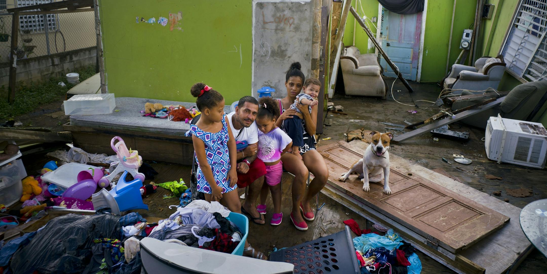 In this Saturday, Oct. 14, 2017 photo, Arden Dragoni, second from left, poses with his wife Sindy, their three children and dog Max, surrounded by what remains of their home destroyed by Hurricane Maria in Toa Baja, Puerto Rico. The Dragoni family has been living in a shelter set up at a school since the storm destroyed their wooden home in late September. They lost everything: clothes, household goods, and an old car. Dragoni supported his family by working construction, but his employers are c