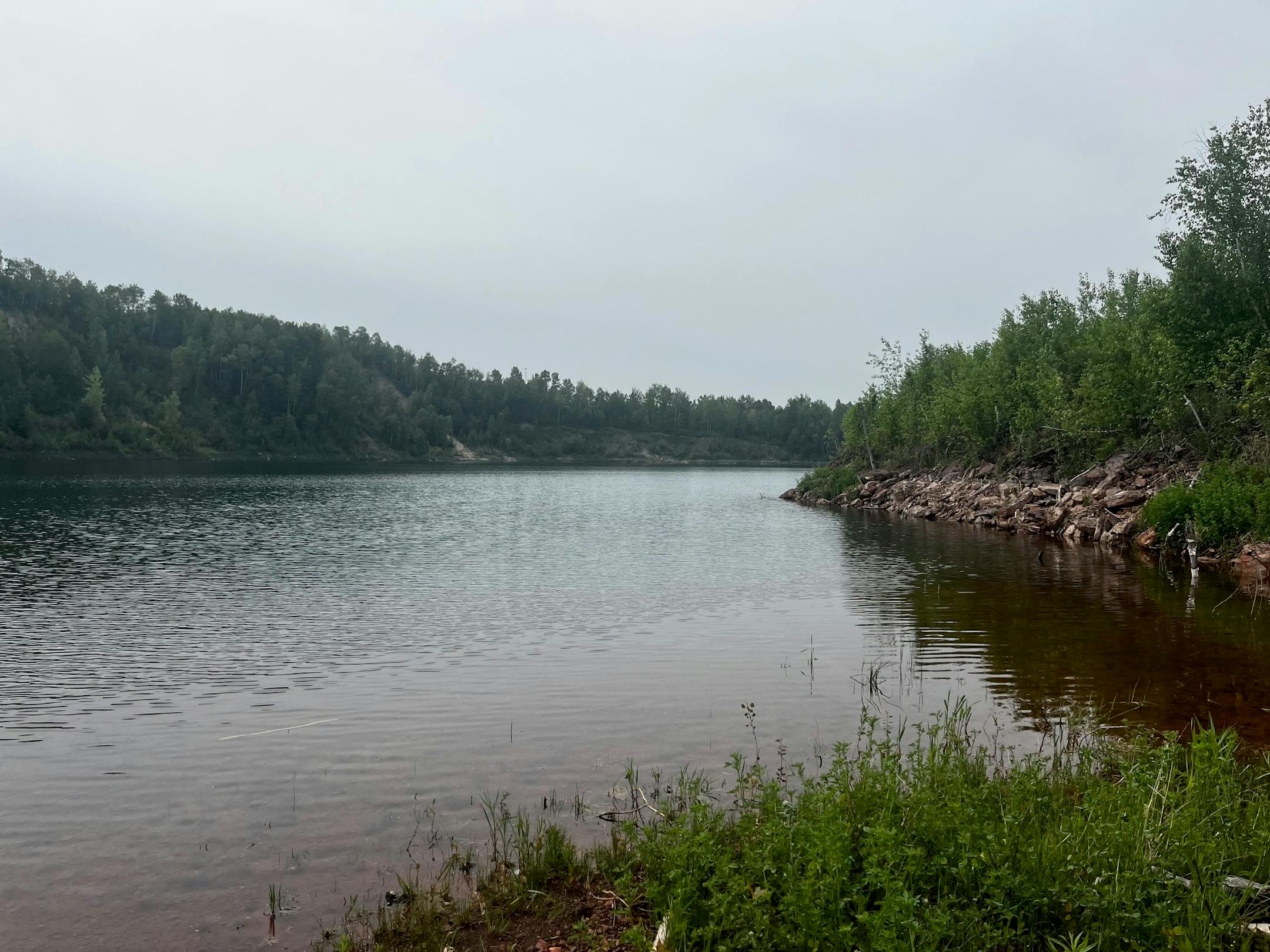 A picture of a mine pit filled with water on an overcast day.