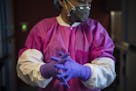 Miao Xu dresses into protective gear before working with the Zika virus in the lab at the National Center for Advancing Translational Sciences, which 