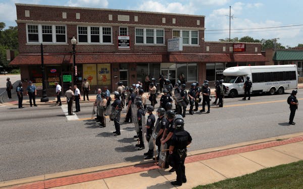 Riot police officers moved down S. Florissant Road in downtown Ferguson, Mo., on Monday, Aug. 11, 2014, as they move demonstrators from the police sta