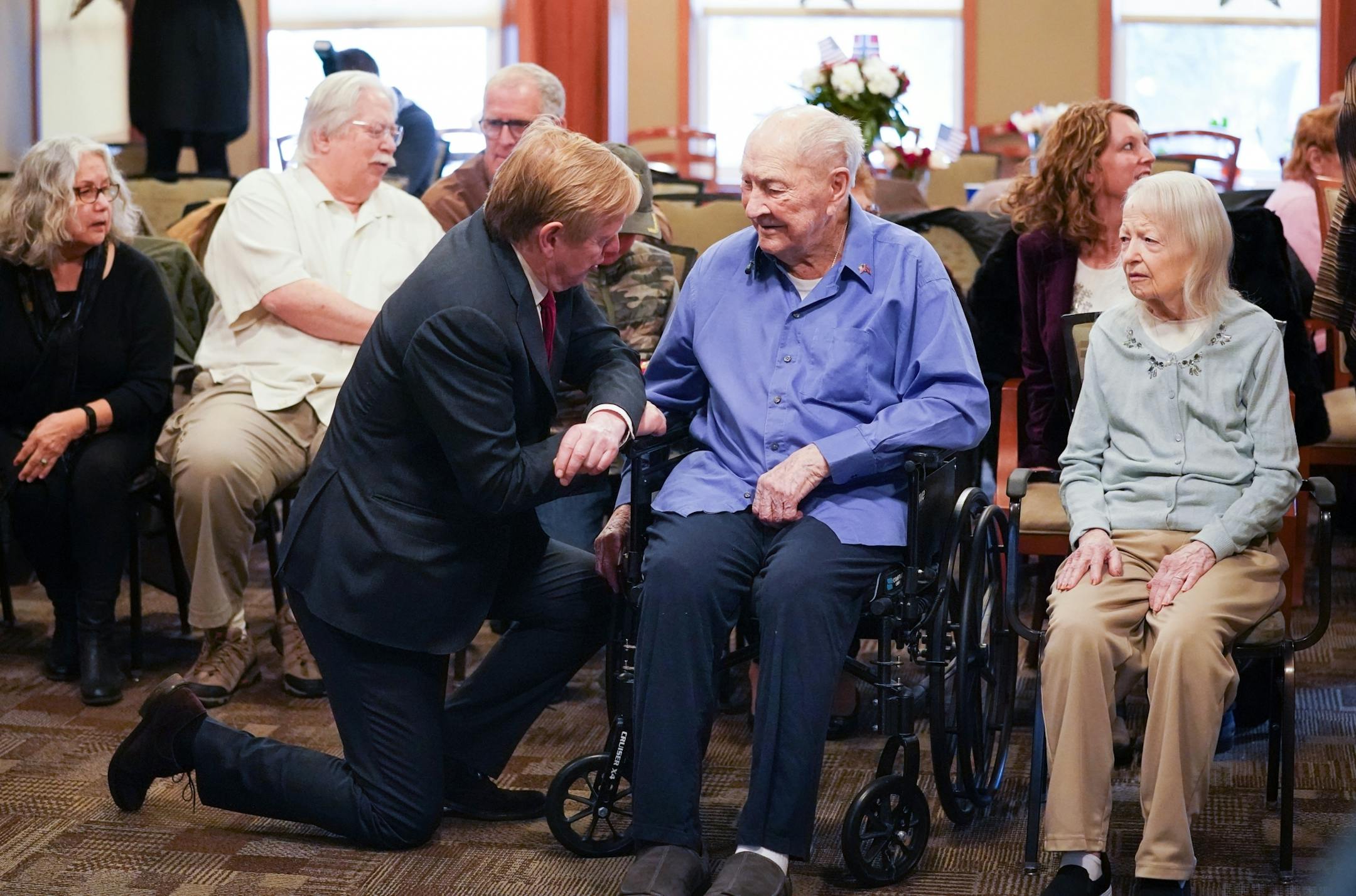 Norwegian Ambassador Kåre R. Aas kneeled down to talk with Wilton Rasmusson after presenting him with two medals. He served under the Office of Strategic Services' Norwegian Operational Unit, NORSO II, during World War II. On the right is Wilton's wife Doris.