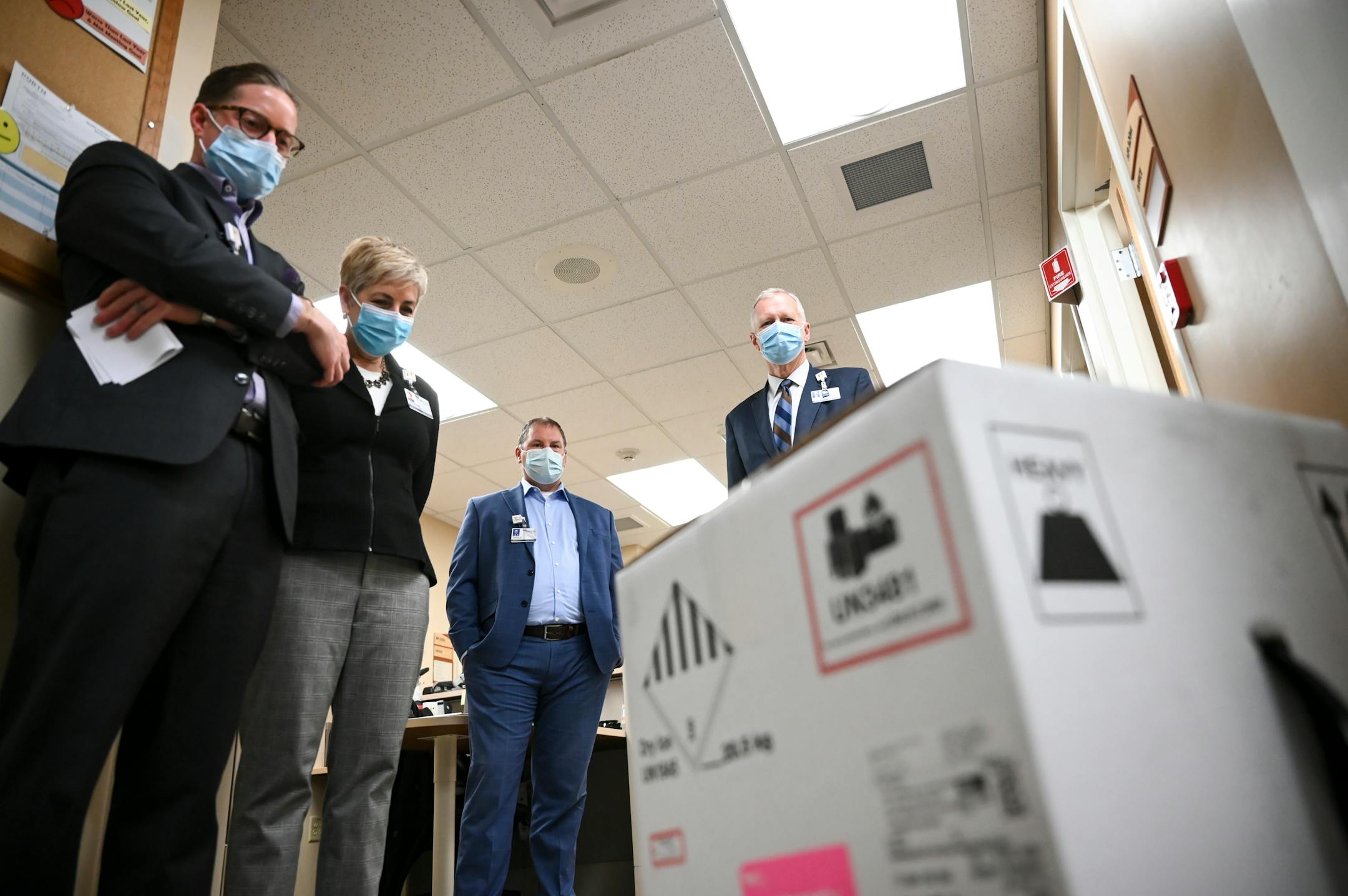 From left, North Memorial Systems Director of Pharmacy Services Paul Krogh, Chief Administrative Officer Samantha Hanson, Vice President of Operations Steve Horstmann and CEO Dr. Kevin Croston took a moment, in silence, and looked at the box containing 975 doses of the COVID-19 vaccine which just arrived at North Memorial Health Hospital Tuesday morning.