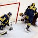 While on his back, the University of Minnesota's Seth Ambroz (17) scores past University of Michigan goalie Zach Nagelvoort (35) during the first peri