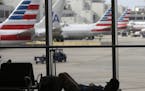 A traveler rests on the floor as American Airlines aircraft are lined up the the gates at Miami International Airport, Tuesday, Nov. 24, 2015, in Miam