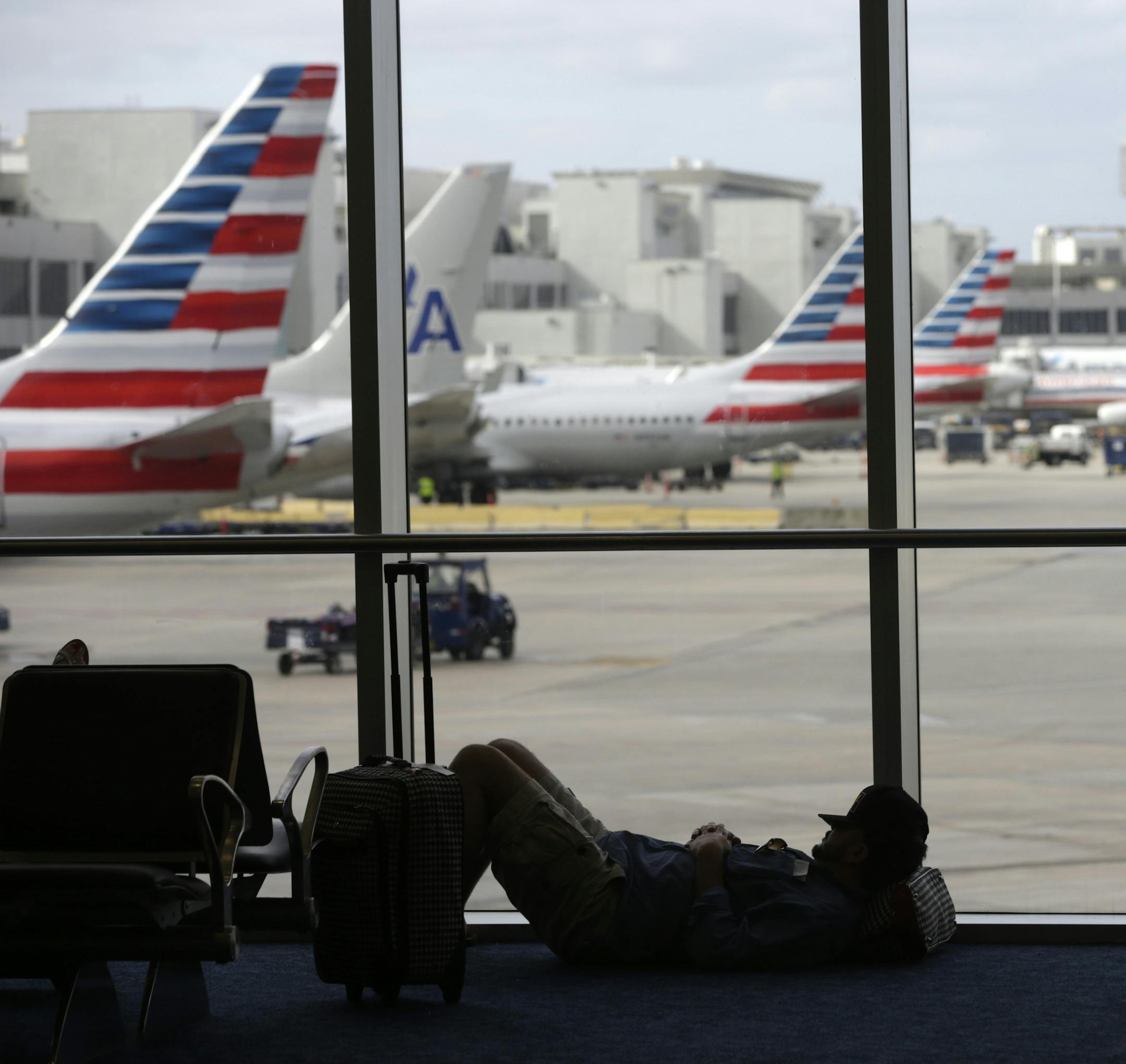 A traveler rests on the floor as American Airlines aircraft are lined up the the gates at Miami International Airport, Tuesday, Nov. 24, 2015, in Miami. Thanksgiving is one of the busiest travel holidays of the year, both in the air and on the roads. (AP Photo/Lynne Sladky)