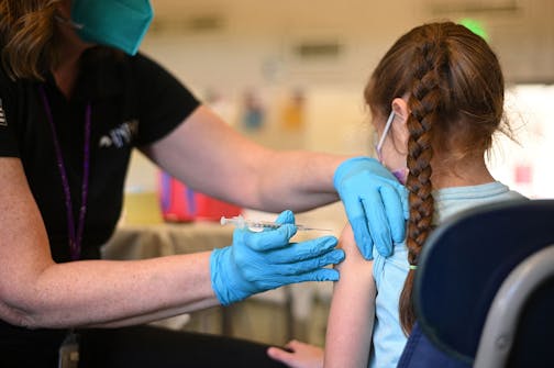 Nurse giving a shot to a girl with braids.