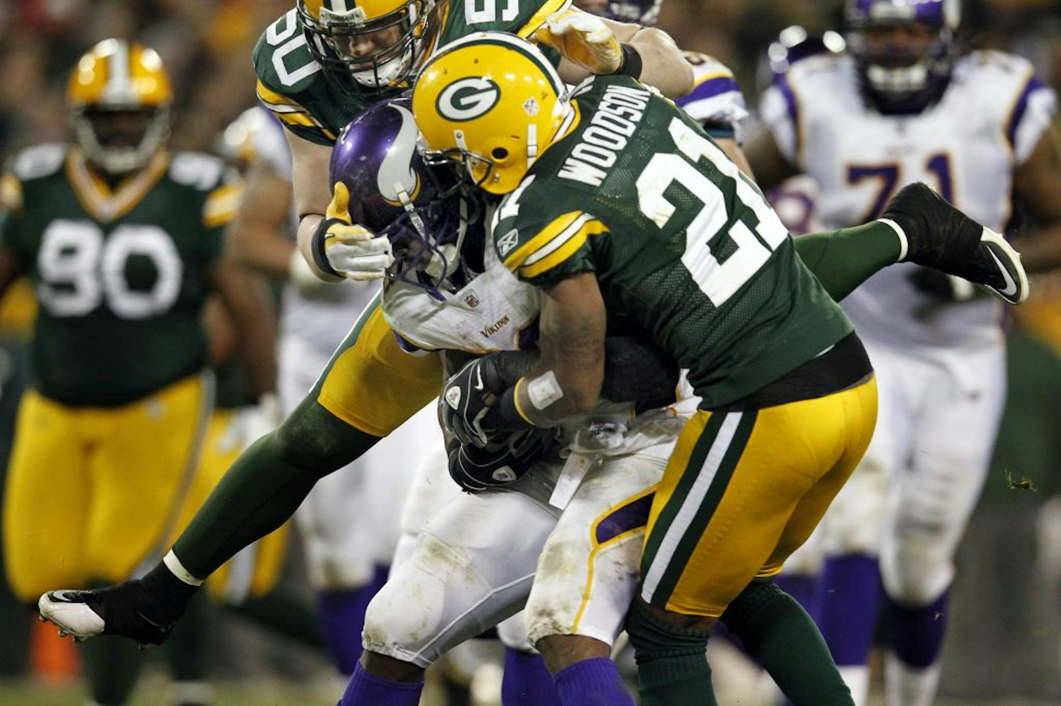 Blitzing Packers cornerback Charles Woodson, left, wrapped up Adrian Peterson, and linebacker A.J. Hawk, top, came in late to complete a 6-yard loss in the third quarter.