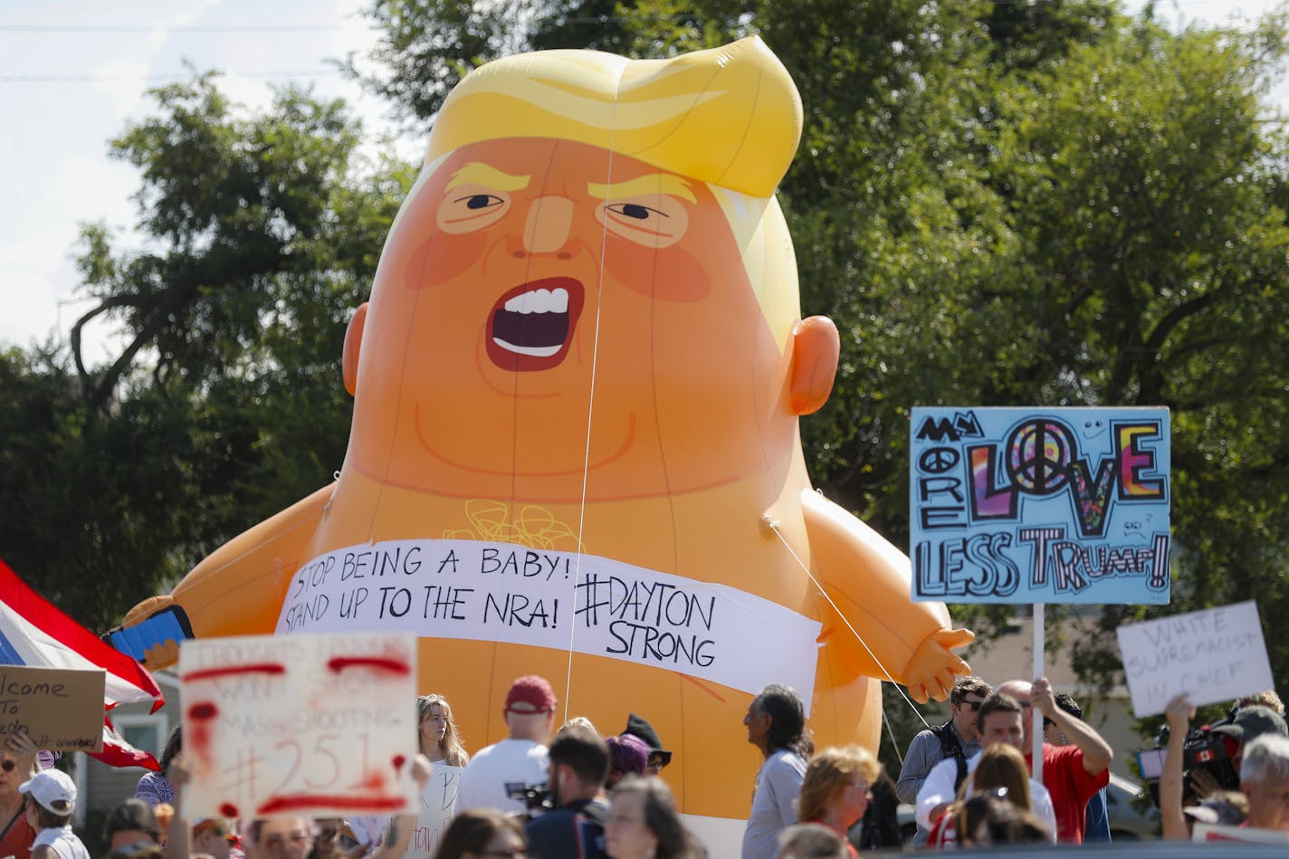 Demonstrators gather in front of an inflatable "Baby Trump" to protest the arrival of President Donald Trump outside Miami Valley Hospital after a mass shooting that occurred in the Oregon District early Sunday morning, Wednesday, Aug. 7, 2019, in Dayton, Ohio. President Donald Trump is headed to Dayton and El Paso, Texas on Wednesday to offer a message of healing and unity, but he will be met by unusual hostility in both places by people who fault his own incendiary words as a contributing caus