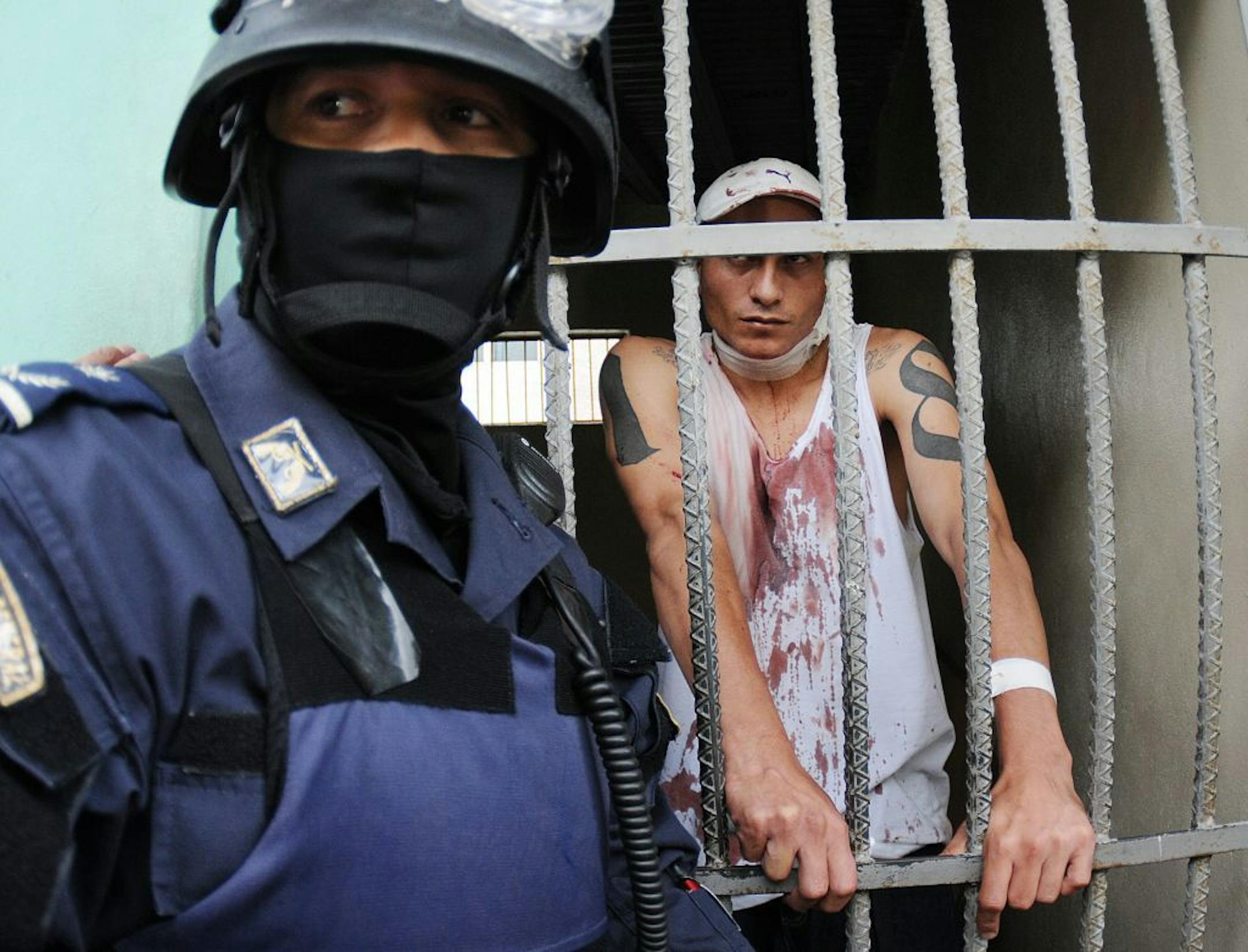 A Honduran police officer guards an injured prisoner, standing inside a cell at the Hospital Escuela, in Tegucigalpa, Honduras, Saturday, Aug. 3, 2013.�Honduran President Porfirio Lobo ordered the militarization of the country�s main prison on Saturday after a riot there left at least three gang members dead and three guards injured. Police said members of the 18 gang clashed with common criminals in Honduras� National Penitentiary, located 10 miles (15 kilometers) north of the capital.