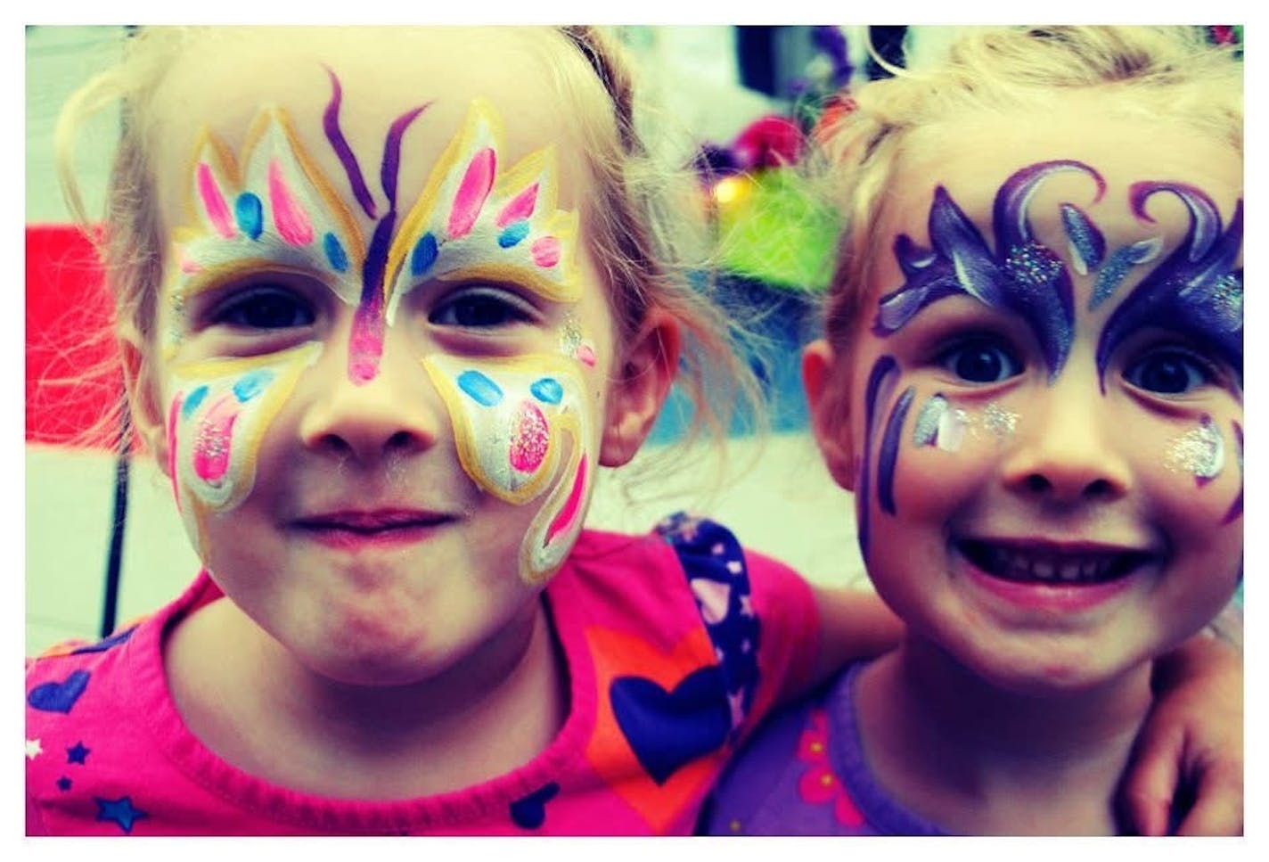 Two kids with colorful face paint smile for the camera.