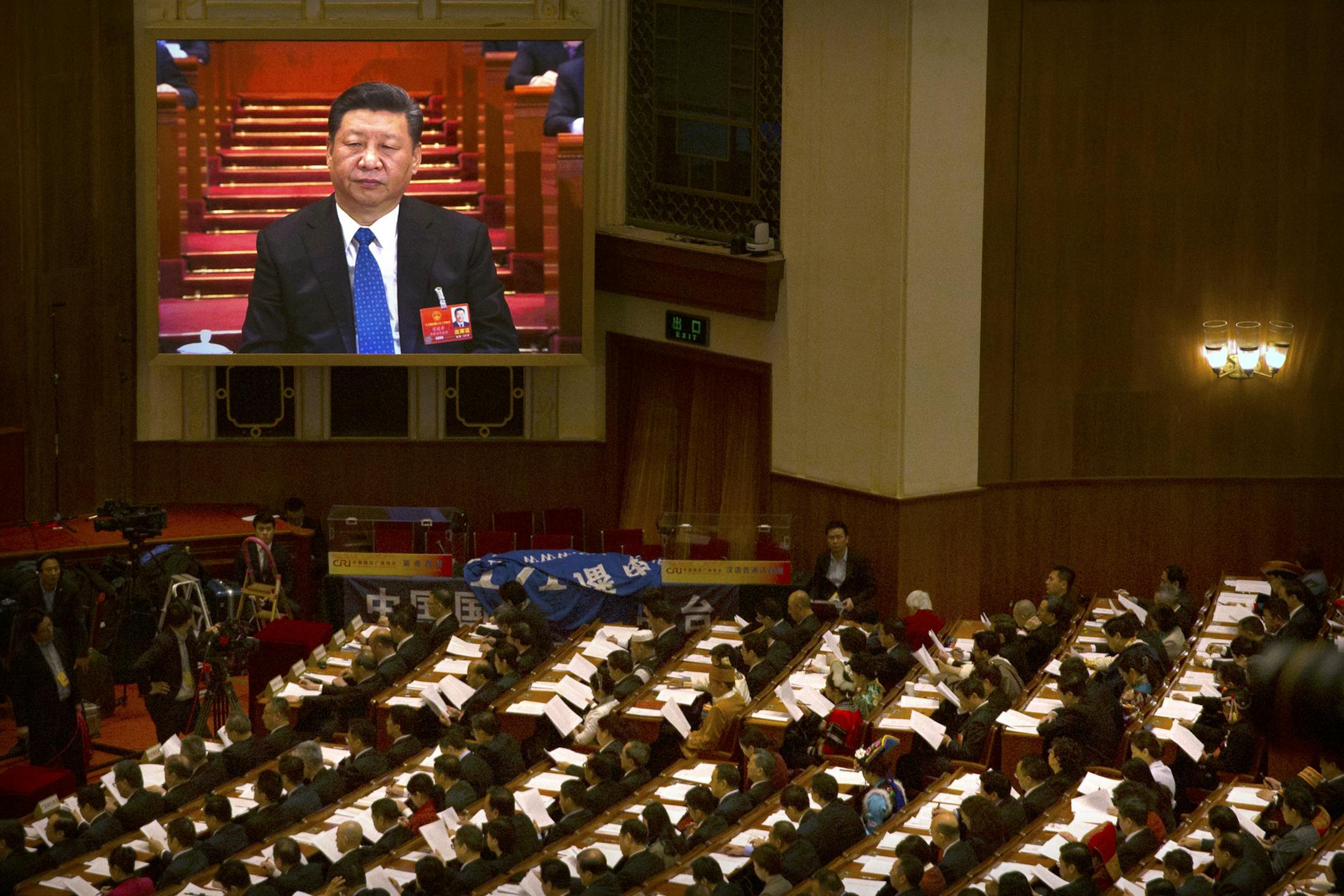 Chinese President Xi Jinping appears on a large screen as delegates read a work report during a plenary session of China's National People's Congress (NPC) in Beijing, Tuesday, March 13, 2018. Chinese President Xi Jinping's anti-corruption campaign stands to gain a major boost as the ceremonial legislature moves to establish a powerful new agency with authority over vast numbers of workers in the public sector. (AP Photo/Mark Schiefelbein)