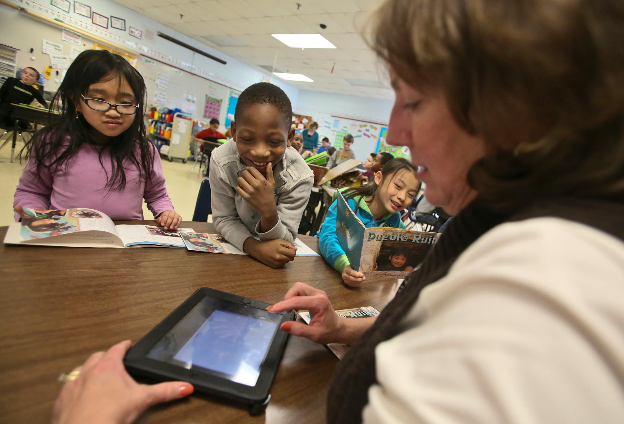 Monroe Elementary School third graders in the ESL program read about Native Americans and their cliff dwellings from a book "Pueblo Ruins." Among the third graders working with teacher Ann Mylrea were Jenny Khon, left to right, Ezekiel Olagunju and Emmy Yang, as Mylrea searched for photographs on a tablet.