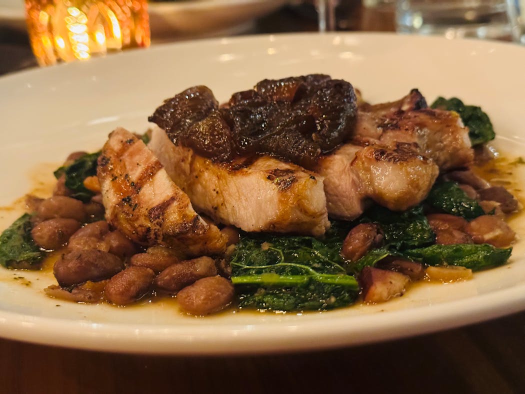 A grilled heritage pork chop on a bed of braised beans and kale at Breva restaurant in Minneapolis' Hotel Ivy.