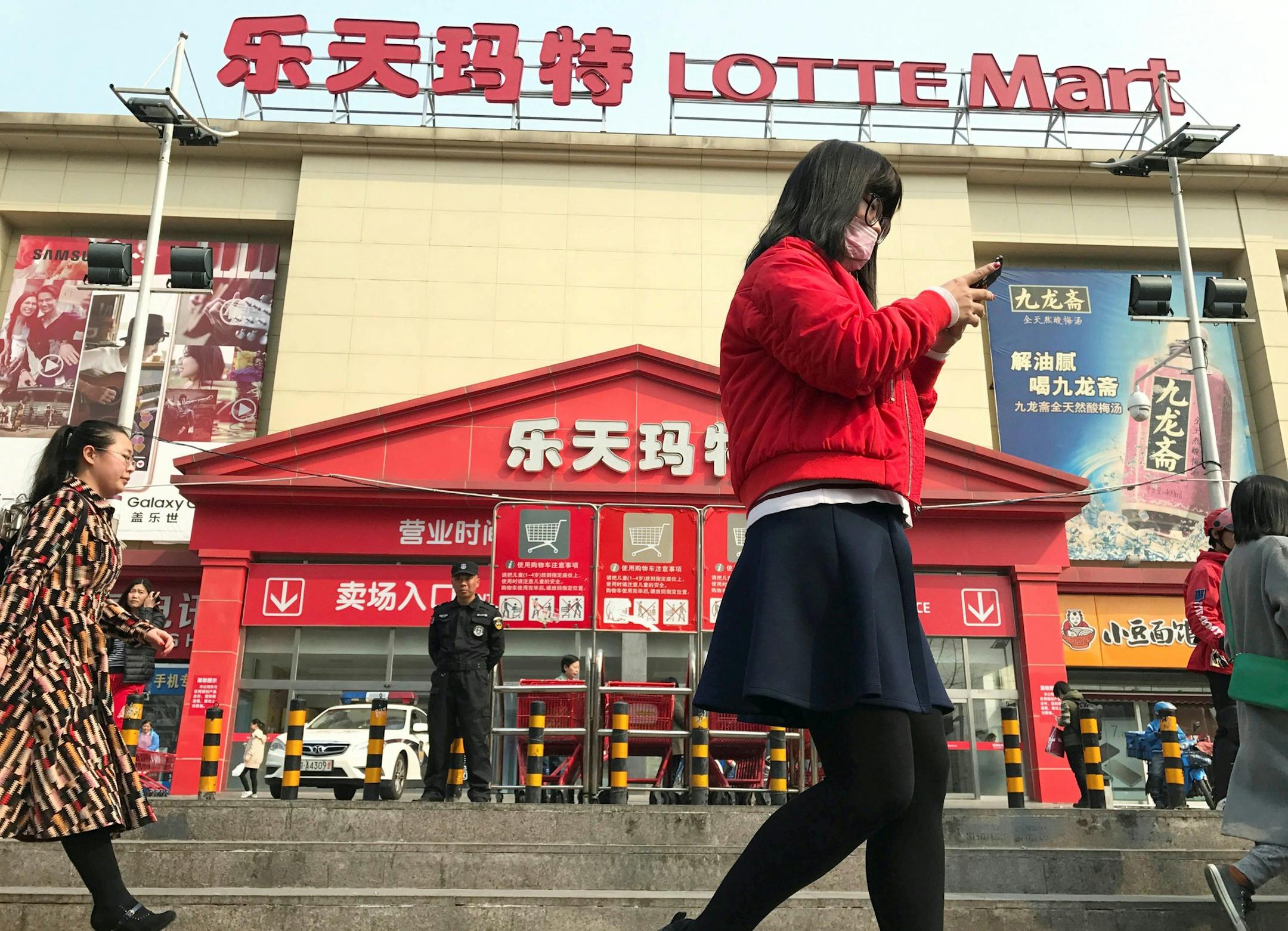 In this Friday, March 17, 2017 photo, residents walk past a Lotte Mart where additional security measures are visible in Beijing, China. Chewing-gum maker and retail giant Lotte Group, South Korea's No. 5 business group, took the brunt of the backlash after agreeing to let one of its golf courses in southeastern South Korea be a site for deploying the Terminal High-Altitude Area Defense system, or THAAD. At least 55 of 99 Lotte Mart discount stores in China were shut in early March for a month e