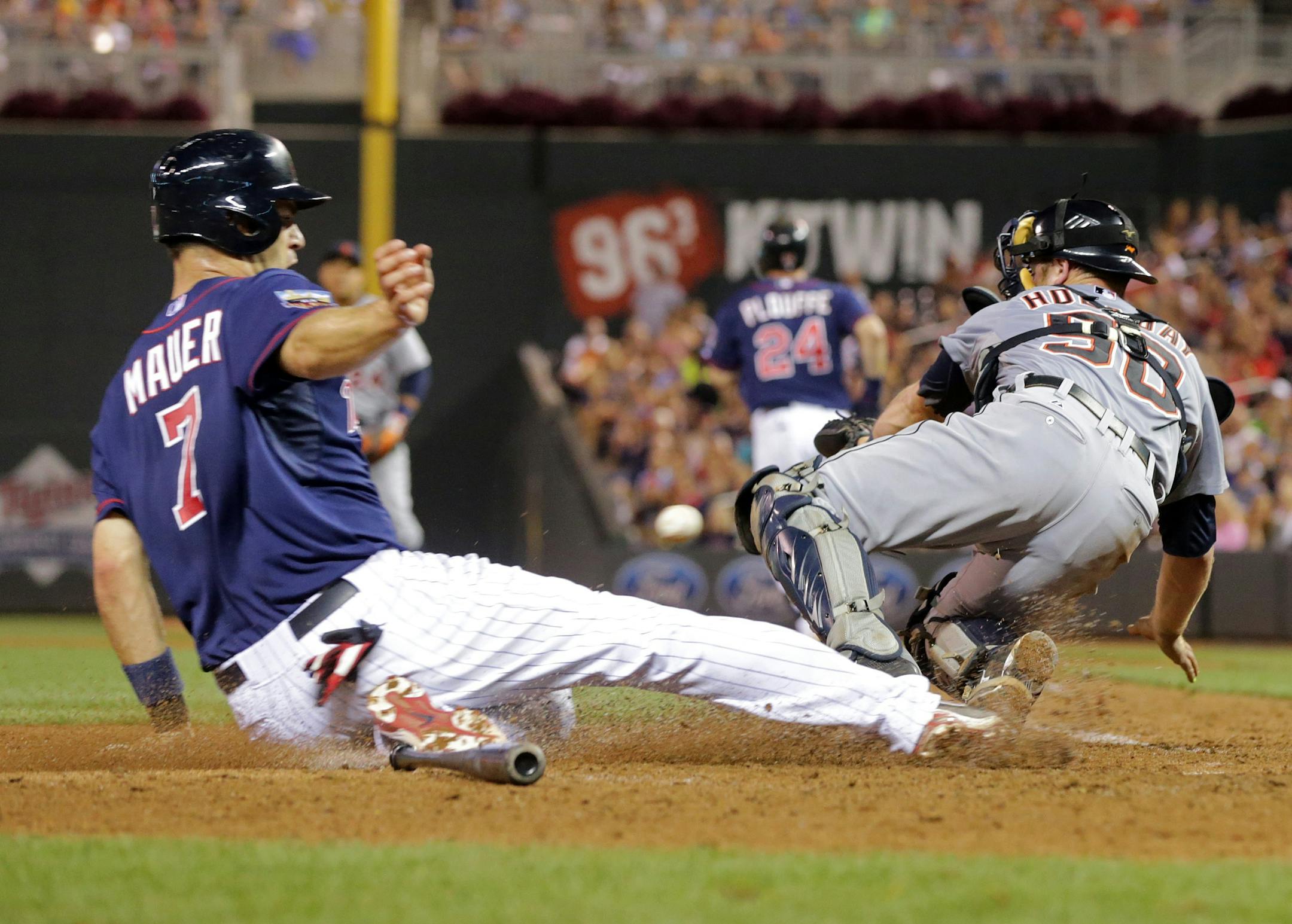 Minnesota Twins' Joe Mauer, left, scores on Trevor Plouffe fielder's choice as Detroit Tigers catcher Bryan Holaday, right, tries to get the wide throw from third baseman Nick Castellanos allowing Twins' Kennys Vargas to score on an error by Castellanos in the sixth inning of a baseball game, Friday, Aug. 22, 2014, in Minneapolis. (AP Photo/Jim Mone)