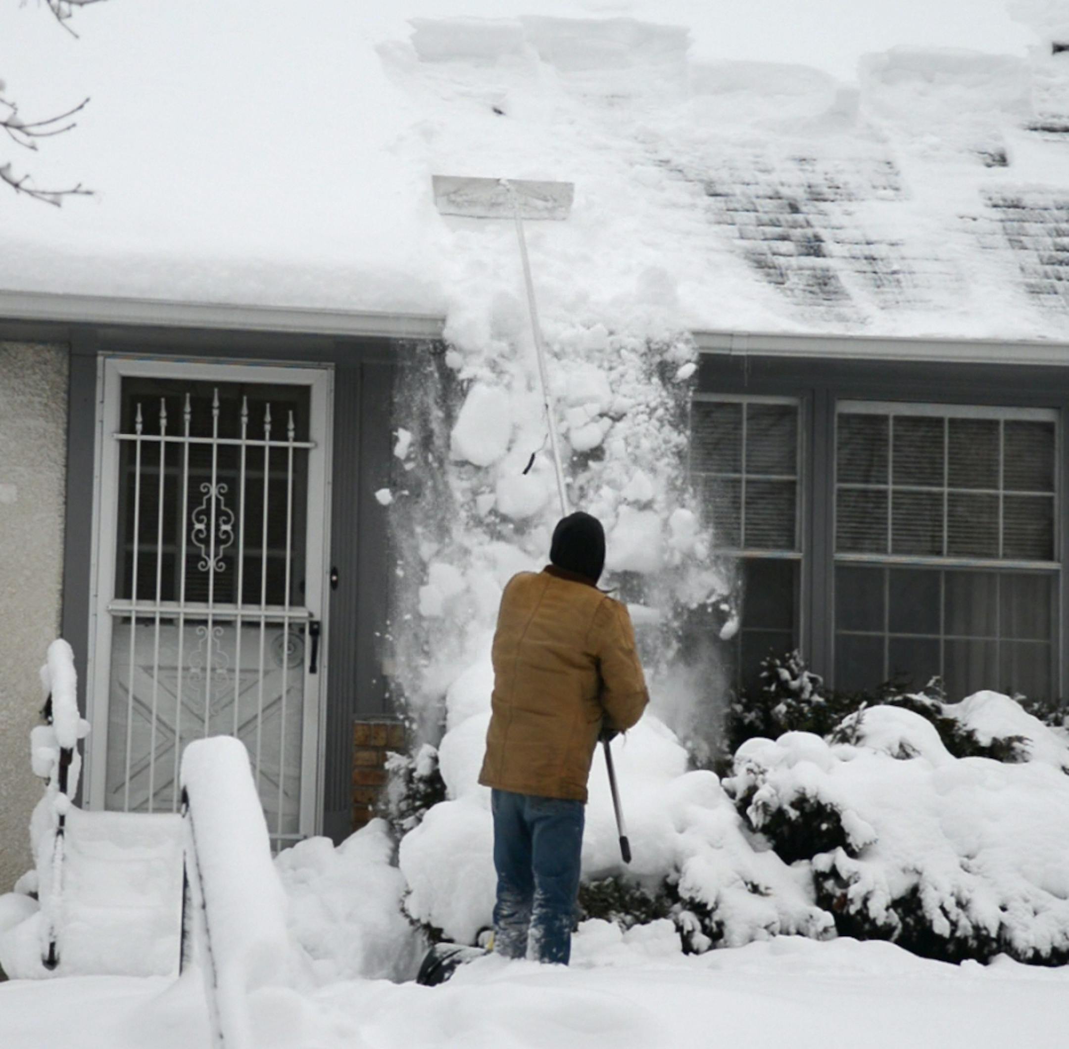 Early Monday Mike Anderson of Minneapolis raked his roof to clear snow from forming ice dams after a storm dumped nearly 16 inches of snow in the Twin Cities metro Sunday, Dec. 9, 2012. Richard Sennott