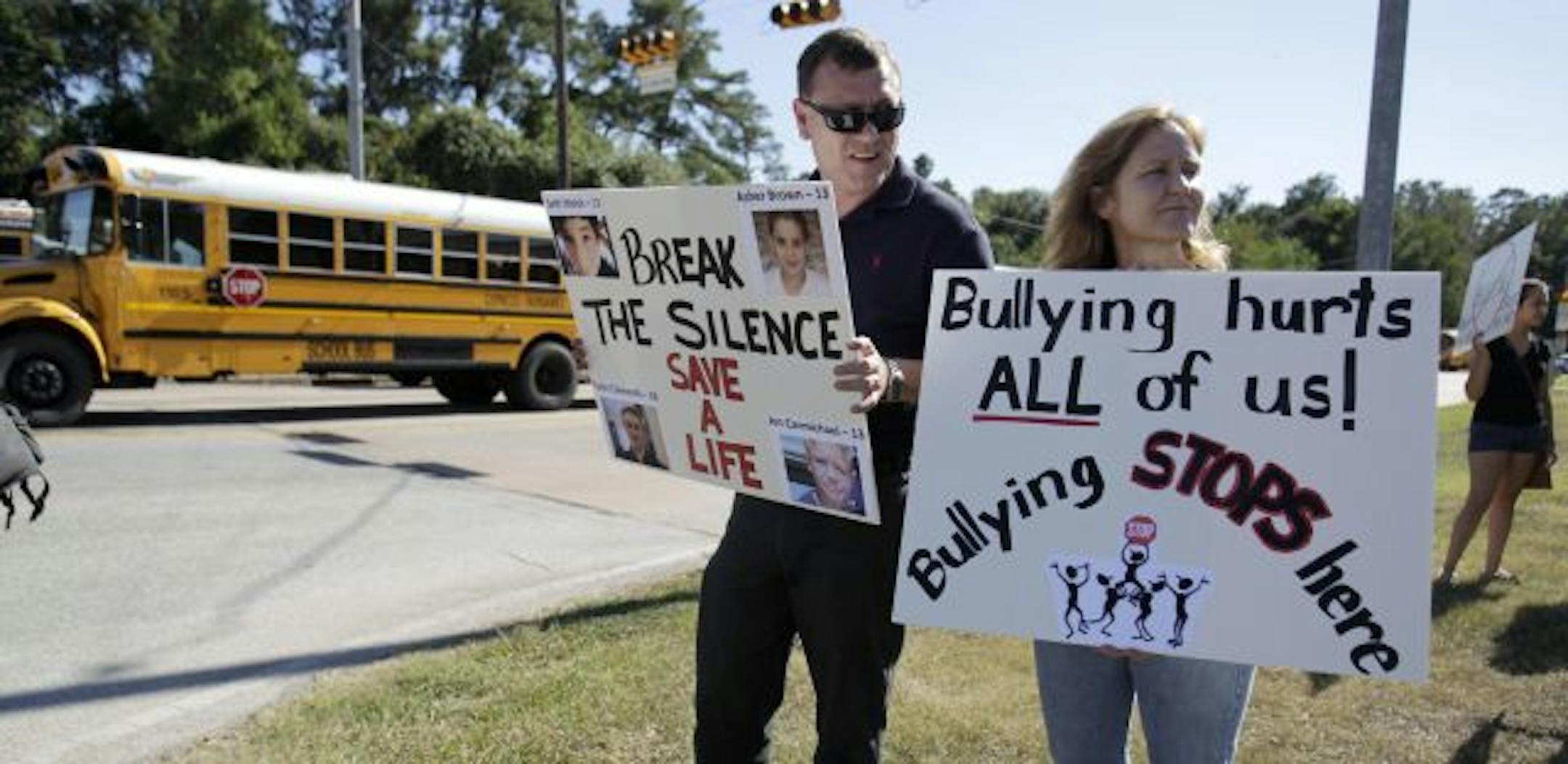 In this Tuesday, Oct. 5, 2010 picture, school buses bring students home from Hamilton Middle School in Cypress, Texas as Brian Carter, left, Sharon Ferranti, foreground right, and others stand on a corner with signs to protest the treatment of Asher Brown, an eighth grader at the school who killed himself at home on Sept. 23, 2010. His parents blamed his suicide on two years of bullying they say he had suffered at the school. A spate of teen suicides linked to anti-gay harassment is prompting sc
