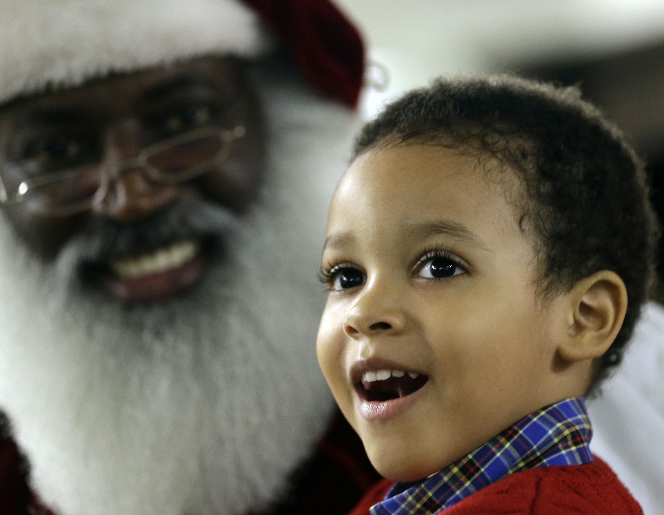 In this Tuesday, Dec. 17, 2013 photo, Dee Sinclair, who bills himself as the real black Santa, delights 4-year-old Joe Morris IV, in Atlanta. Fusing the icon of the long-white beard and red suit from American artist Norman Rockwell and later Coca-Cola, in recent years the new Santas incorporate their own ethnic take on the Christmastime figure with various interpretations. (AP Photo/John Bazemore)